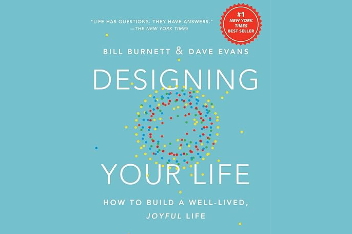 Hardcover book titled "Designing Your Life: How to Build a Well-Lived, Joyful Life" by Bill Burnett & Dave Evans. The blue cover features the words “DESIGNING YOUR LIFE” in large white letters, overlaid with concentric circles of yellow dots on the outside, blue dots for next ring, and red dots for the innermost ring.